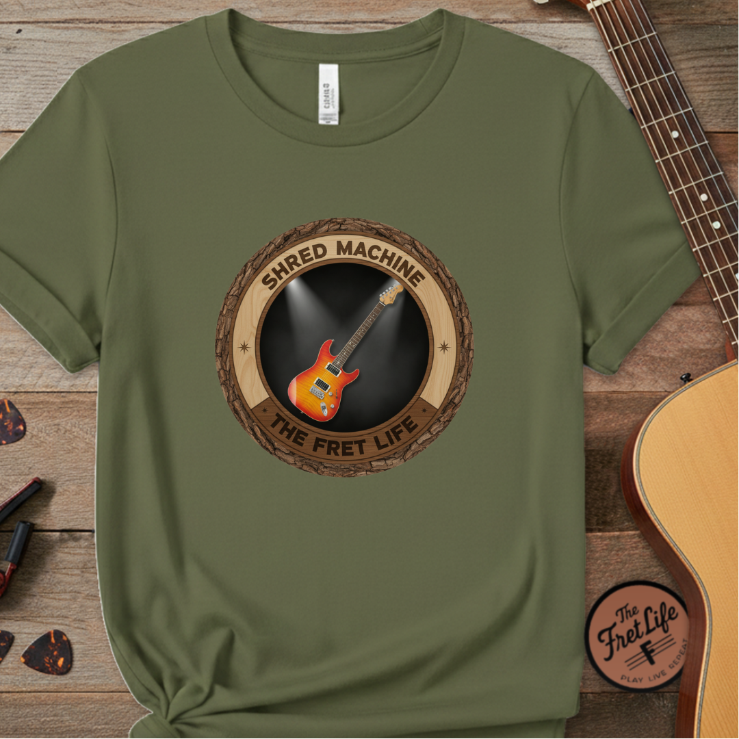 Green t-shirt with 'Shred Machine' graphic on a wooden surface with a guitar.