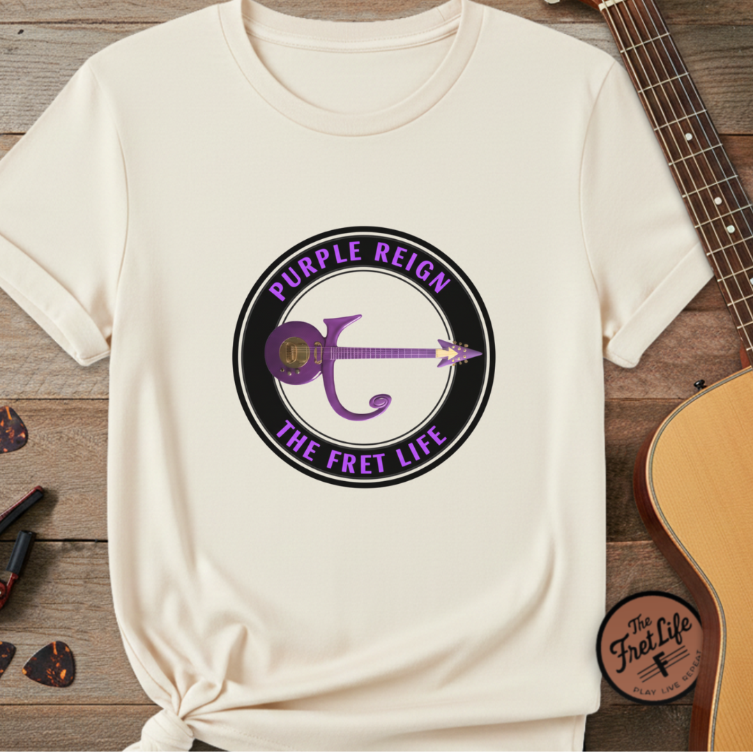 White t-shirt with 'Purple Reign The Fret Life' design on a wooden surface with a guitar.
