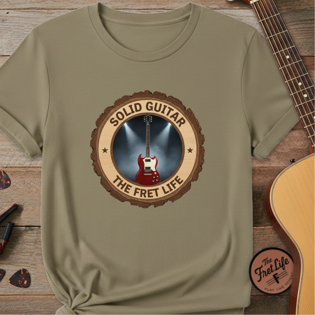 Khaki t-shirt with 'Solid Guitar The Fret Life' design on a wooden surface with a guitar.