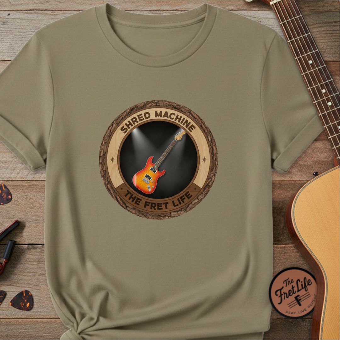Green t-shirt with 'Shred Machine' graphic on a wooden surface with a guitar