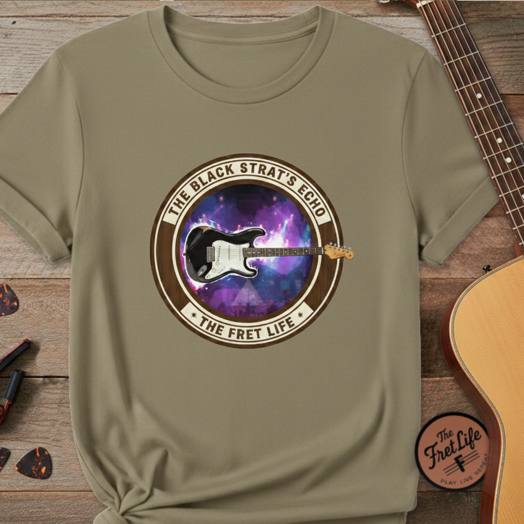 Khaki t-shirt with guitar graphic and text on a wooden surface with a guitar.