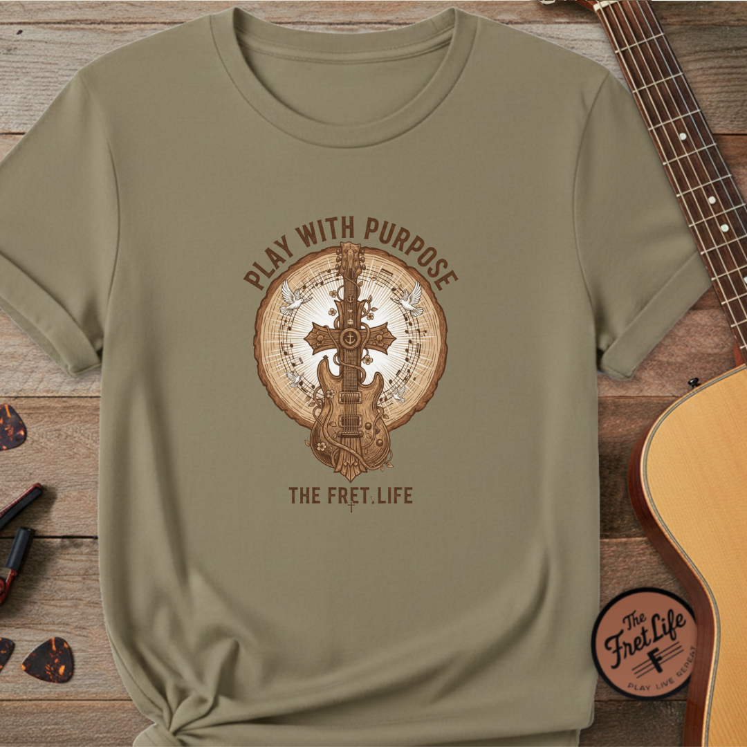 Khaki t-shirt with guitar graphic and 'Play with Purpose' text on a wooden surface with a guitar.