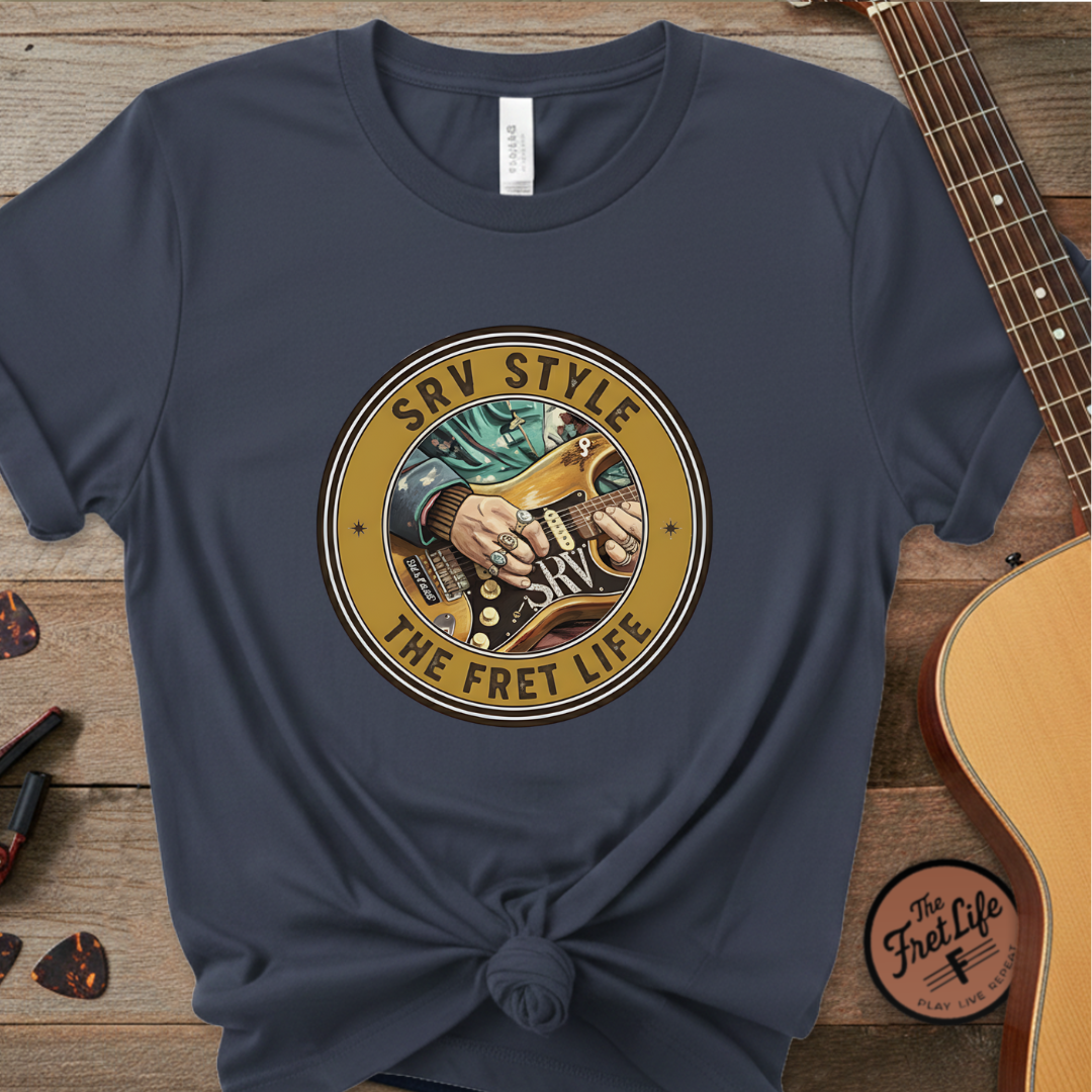 Navy blue t-shirt with 'SRV Style The Fret Life' graphic on a wooden surface with a guitar.