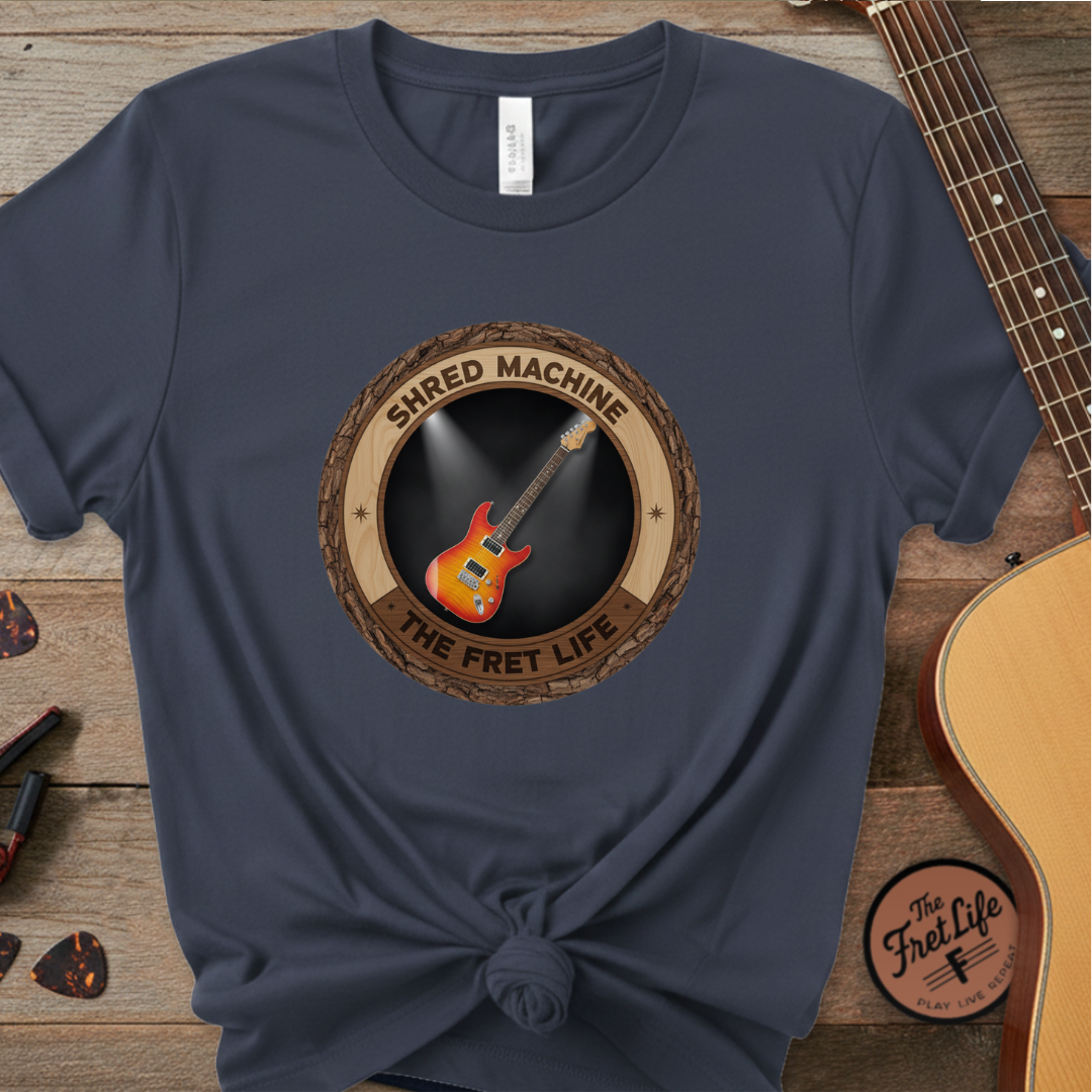 Navy blue t-shirt with 'Shred Machine' graphic on a wooden surface with guitars.