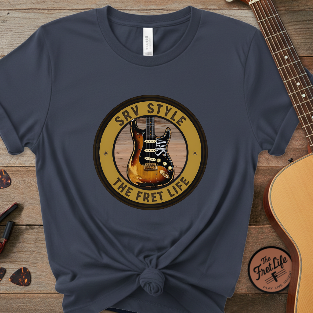 Navy blue t-shirt with guitar graphic and text on a wooden surface with guitars.