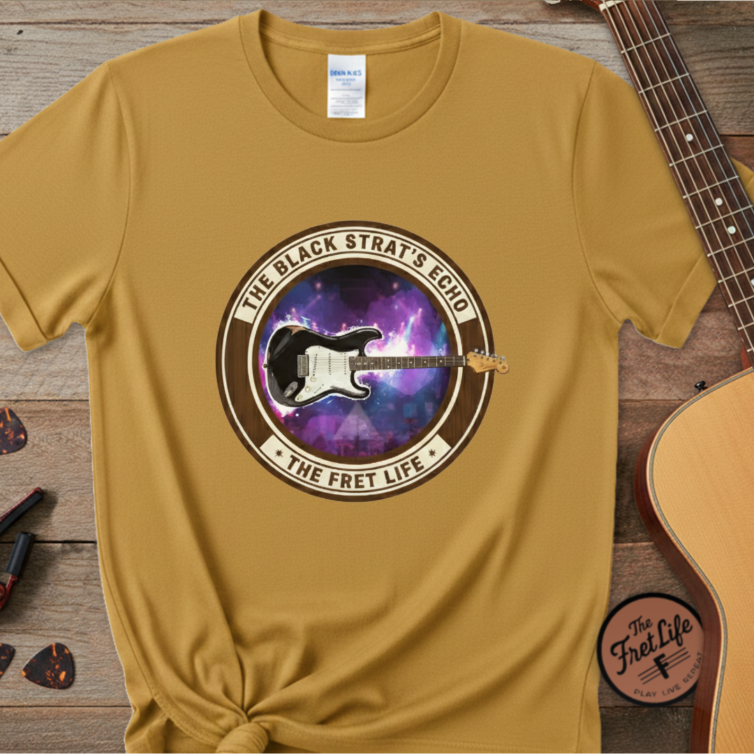 Mustard yellow t-shirt with guitar graphic and text on a wooden surface with a guitar.