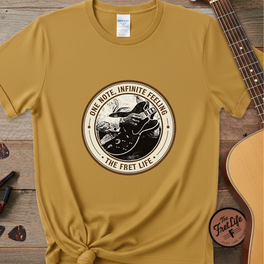 Yellow t-shirt with 'The Fret Life' graphic design on a wooden surface with a guitar.