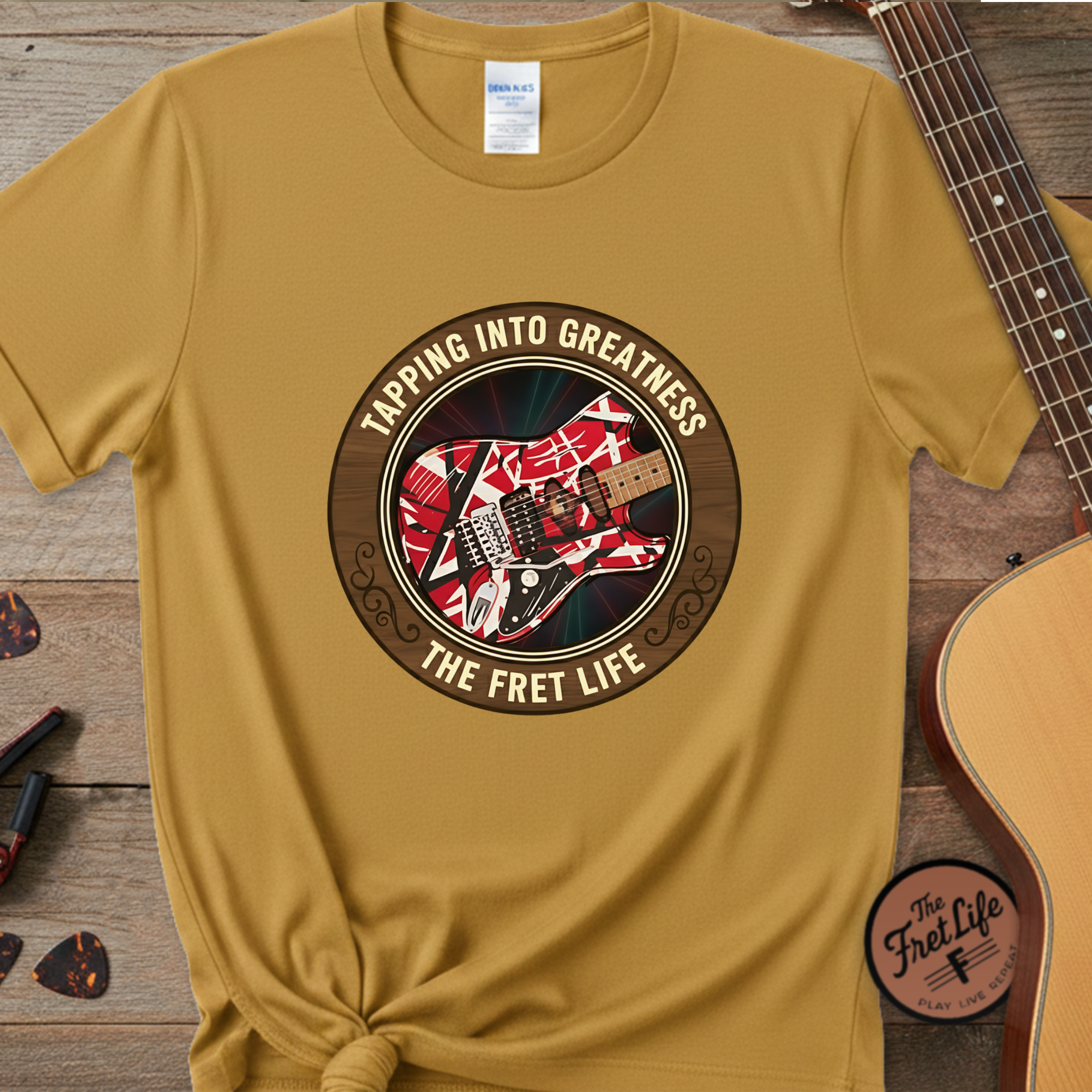Yellow t-shirt with guitar graphic and text 'Tapping into Greatness, The Fret Life' on a wooden surface with a guitar.