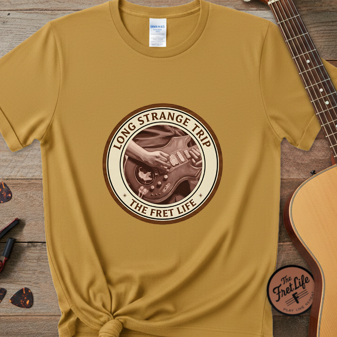 Yellow t-shirt with 'Long Strange Trip: The Fret Life' design on a wooden surface with a guitar.