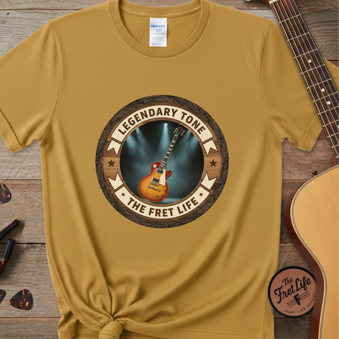 Yellow t-shirt with 'Legendary Tone: The Fret Life' graphic on a wooden surface with a guitar.