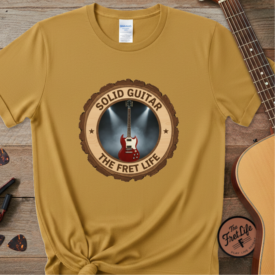 Yellow t-shirt with a guitar graphic and text on a wooden surface with a guitar.