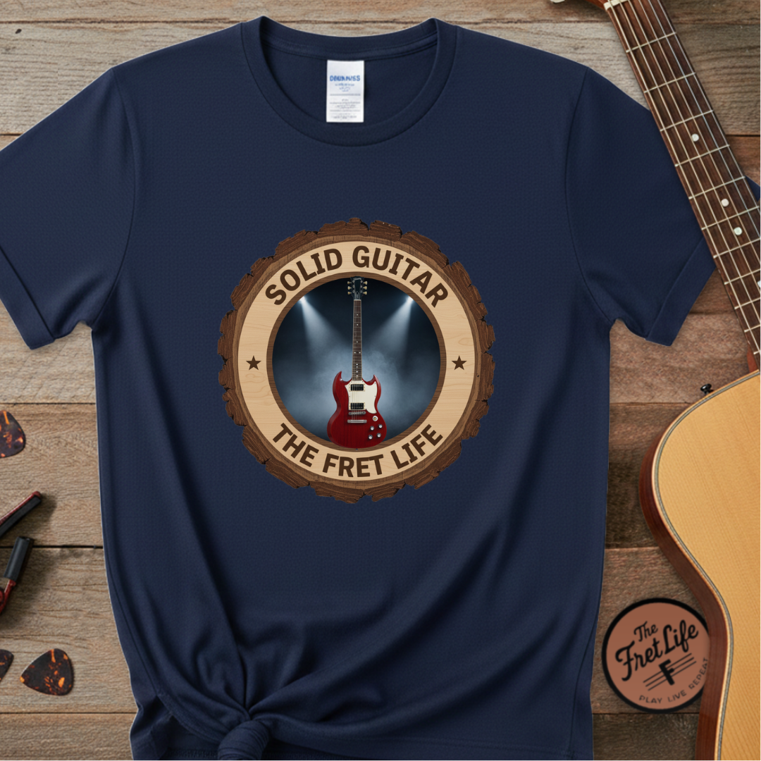 Navy blue t-shirt with 'Solid Guitar The Fret Life' design on a wooden surface with guitars.