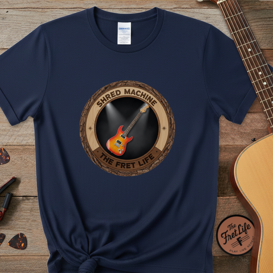 Navy blue t-shirt with 'Shred Machine' graphic on a wooden surface with guitars.