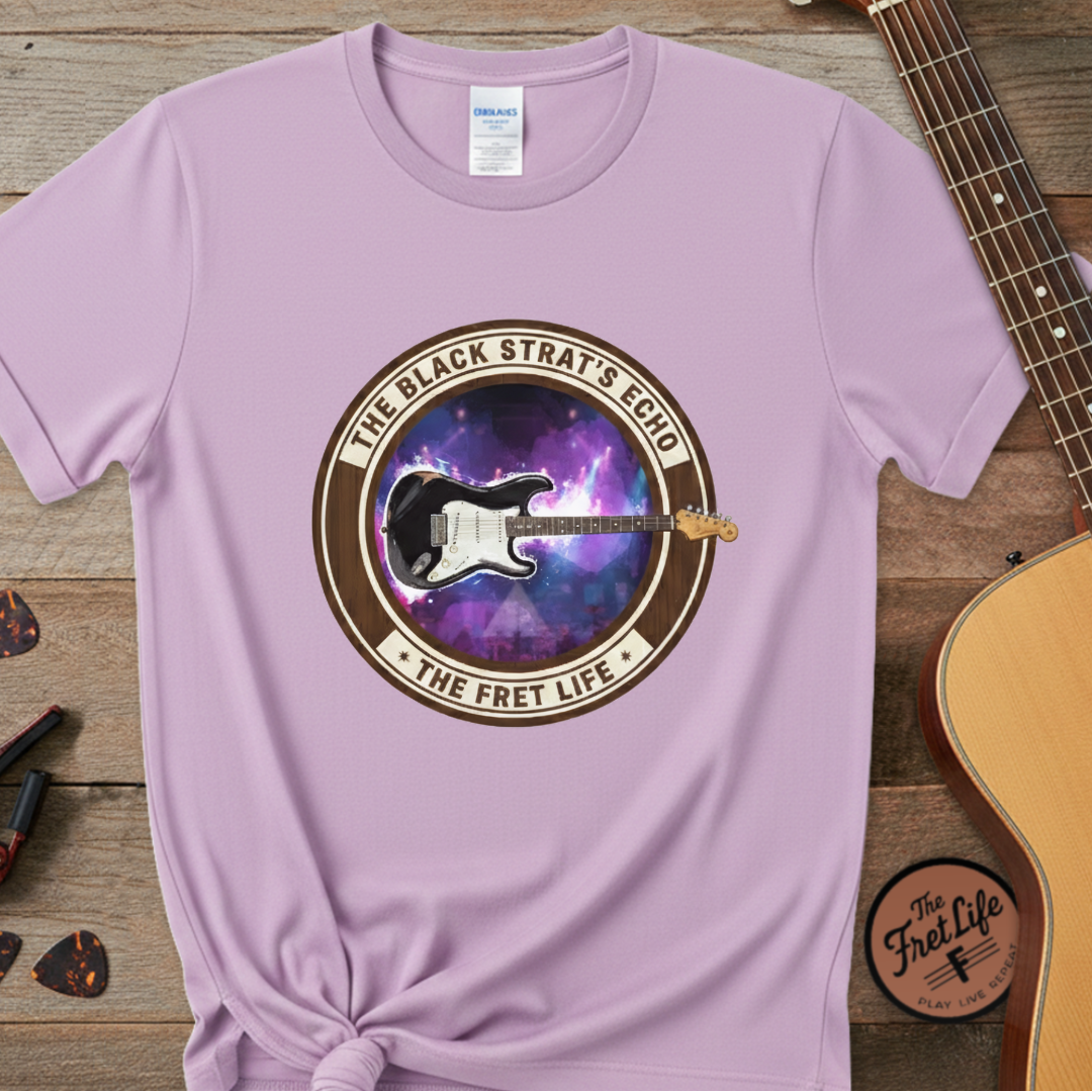 Purple t-shirt with guitar graphic and text on a wooden surface with a guitar and pick.