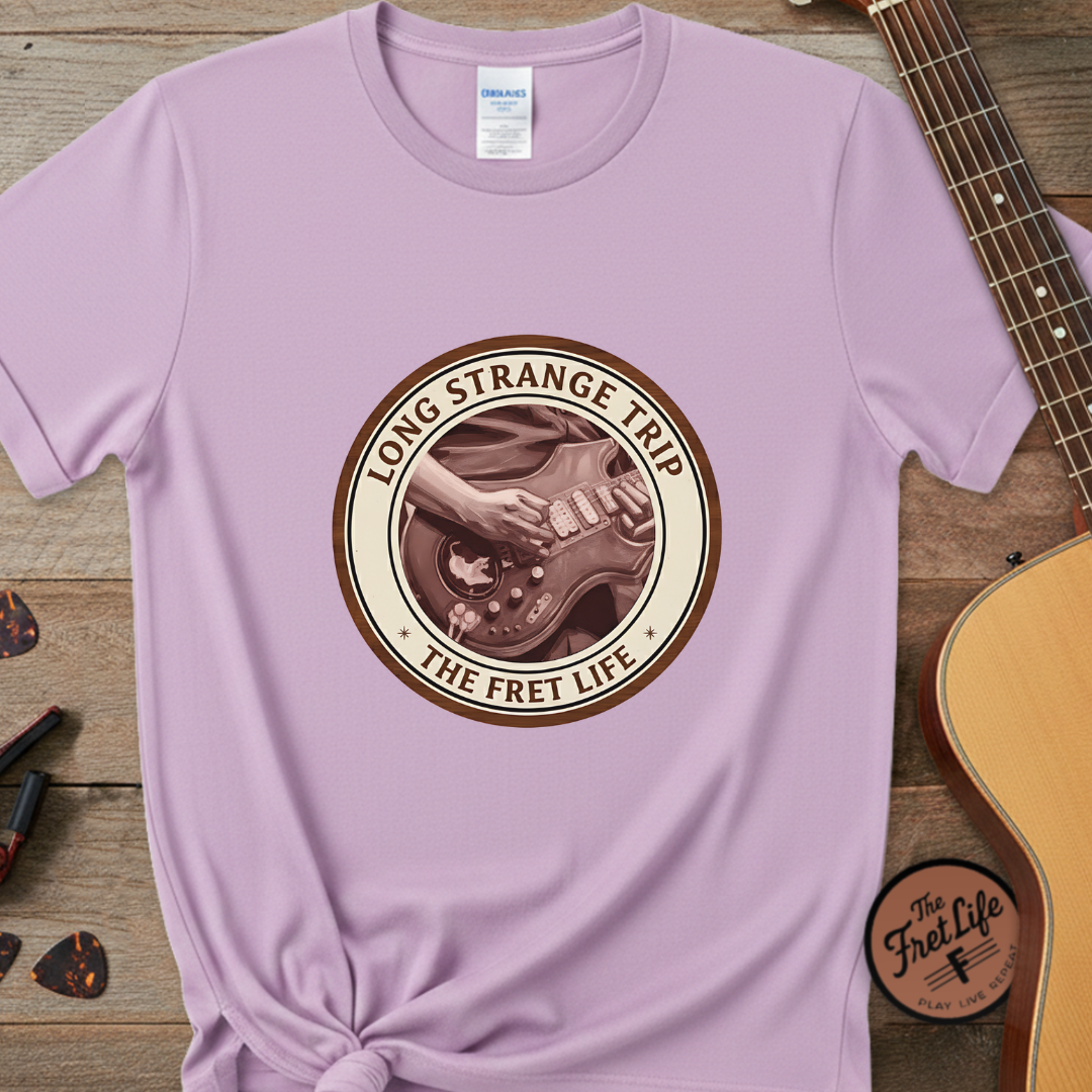 Purple t-shirt with 'Long Strange Trip: The Fret Life' design on a wooden surface with a guitar.