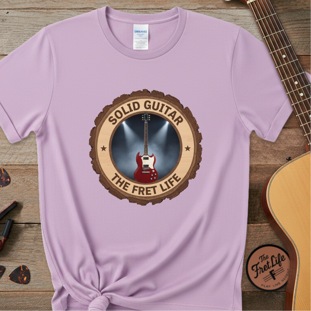 Purple t-shirt with 'Solid Guitar The Fret Life' design on a wooden surface with a guitar.