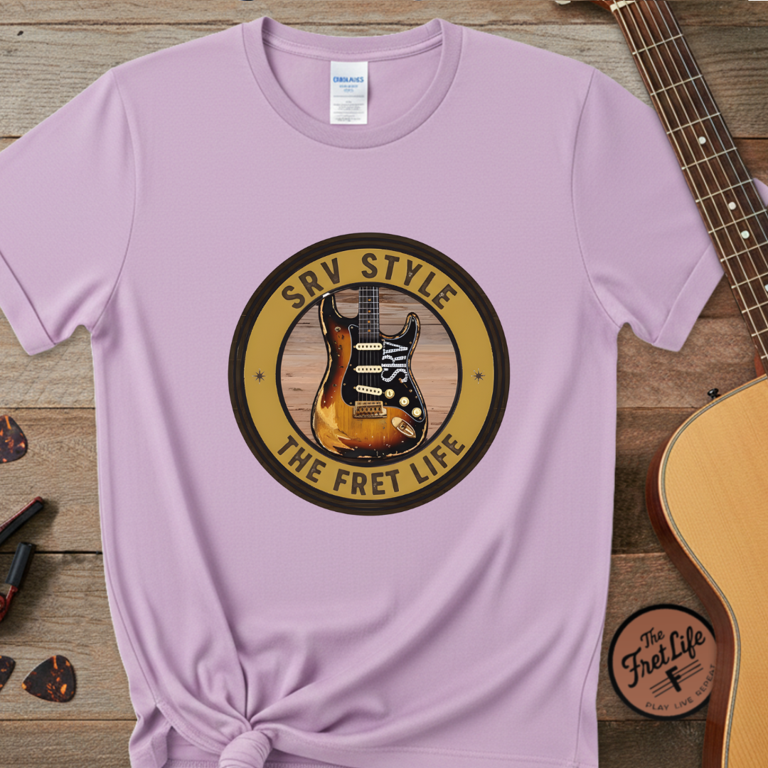 Purple t-shirt with guitar graphic and text on a wooden surface with a guitar and pick.