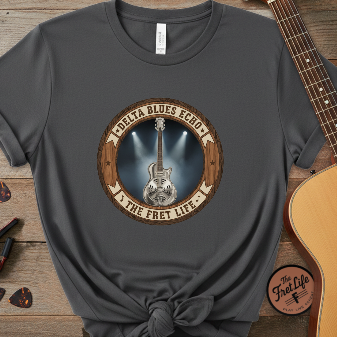 Gray t-shirt with guitar graphic and text on a wooden surface with a guitar