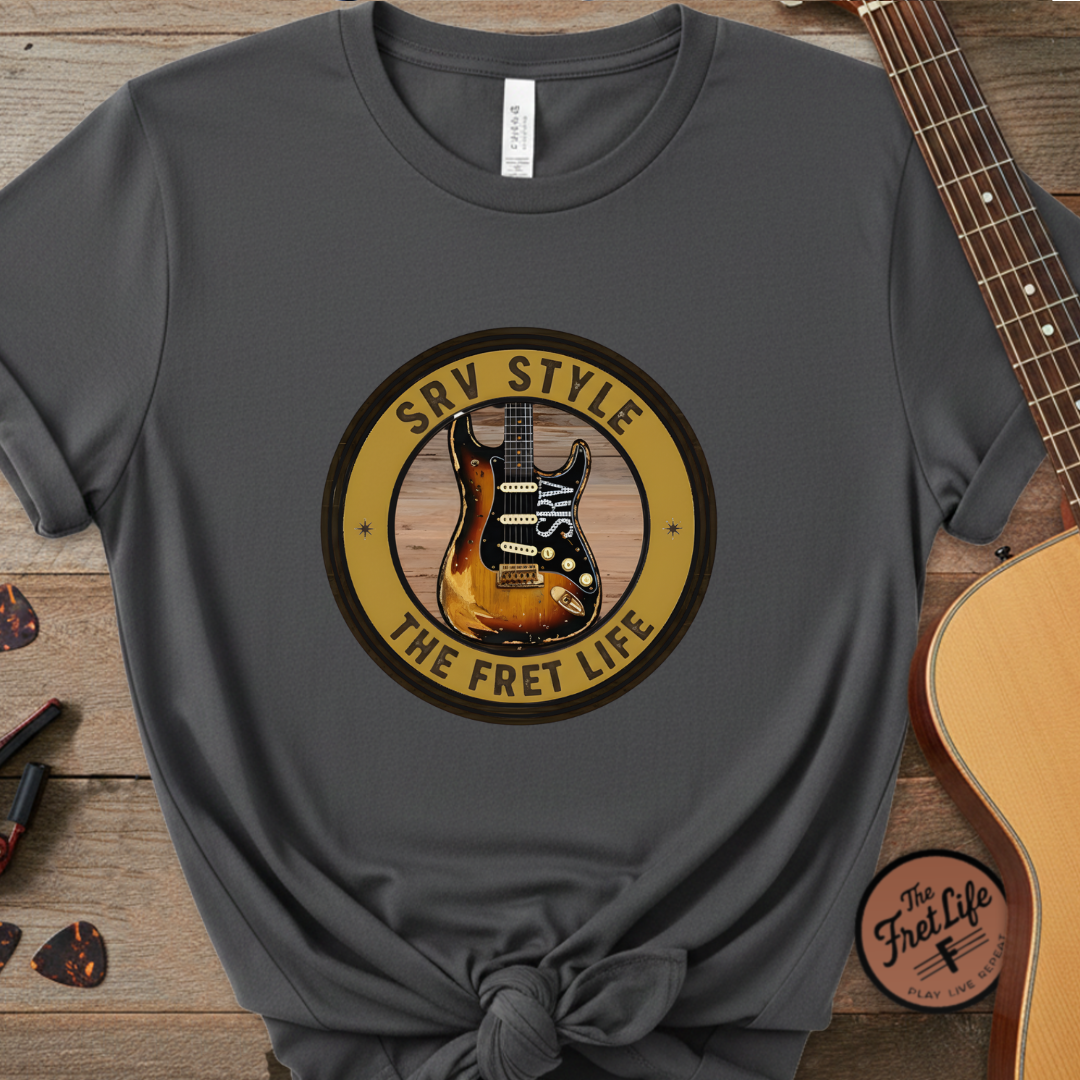 Gray t-shirt with guitar graphic and text on a wooden surface with a guitar.