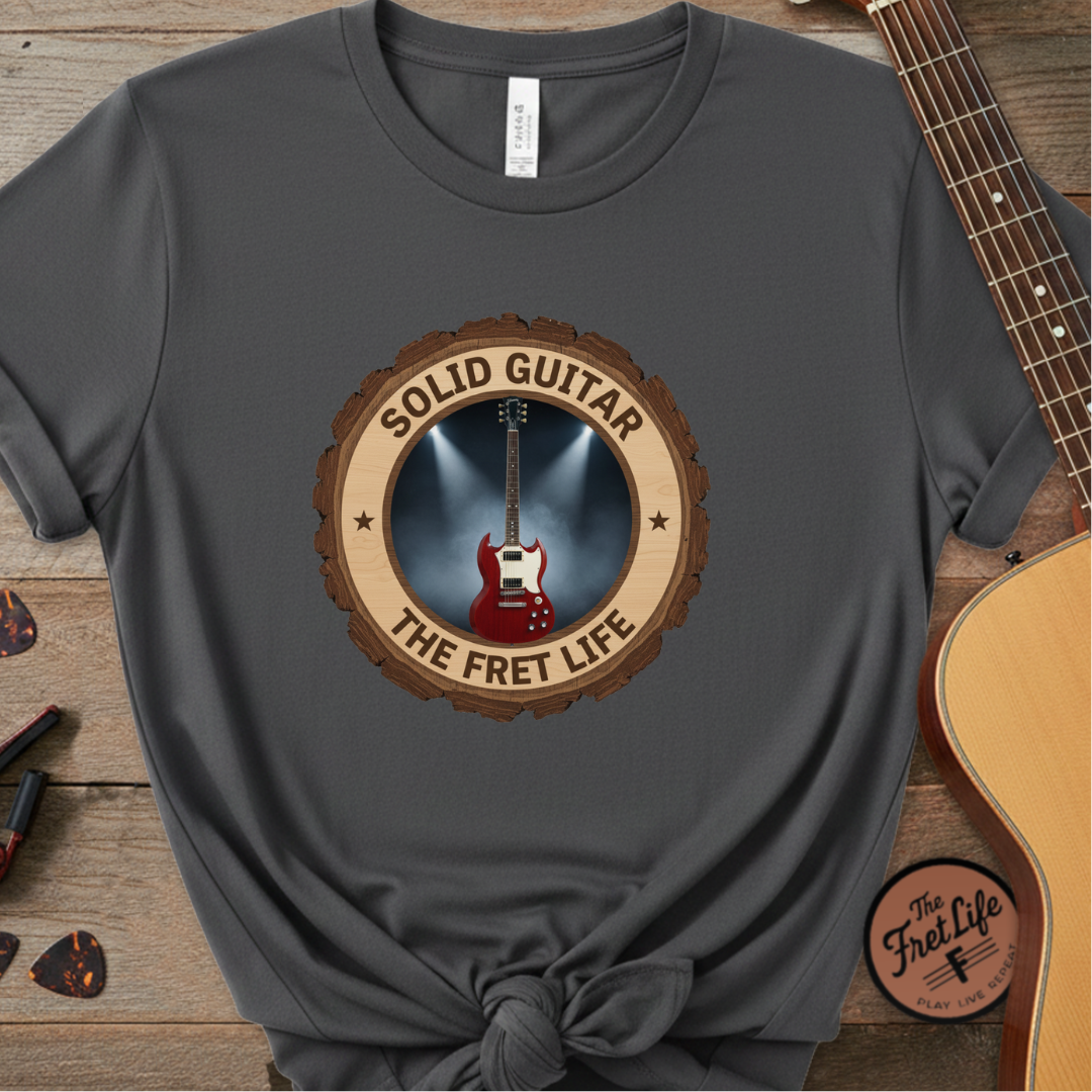 Gray t-shirt with 'Solid Guitar The Fret Life' design on a wooden surface with a guitar.