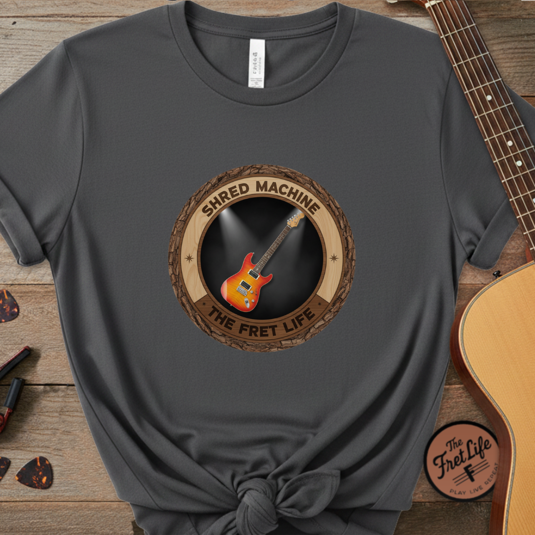 Gray t-shirt with 'Shred Machine' graphic on a wooden surface with a guitar