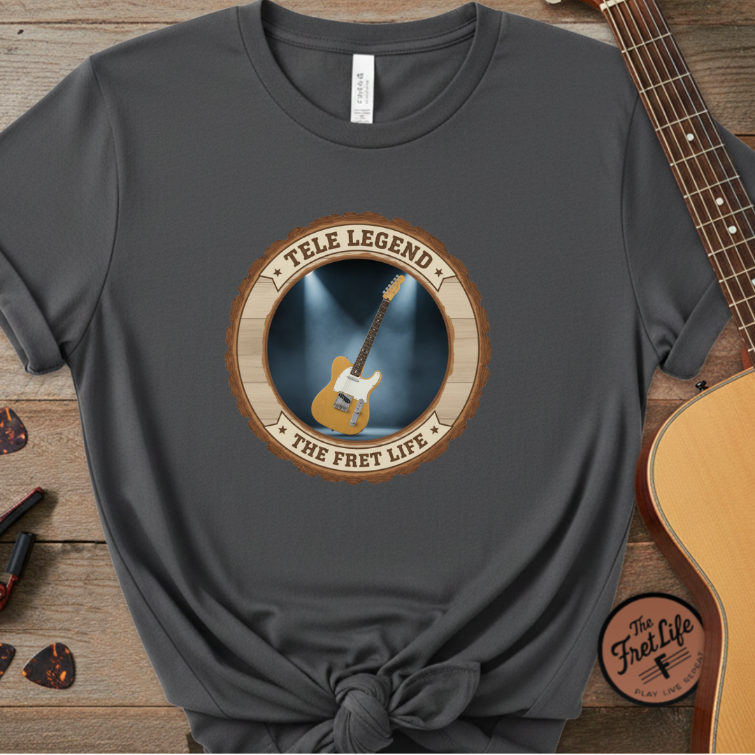 Gray t-shirt with guitar graphic and text on a wooden surface with a guitar.