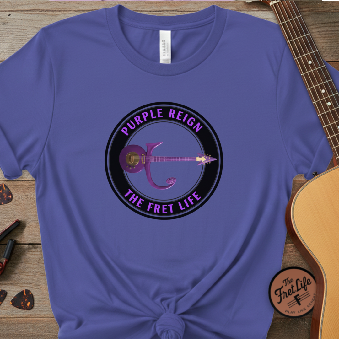 Blue t-shirt with 'Purple Reign The Fret Life' design on a wooden surface with a guitar.