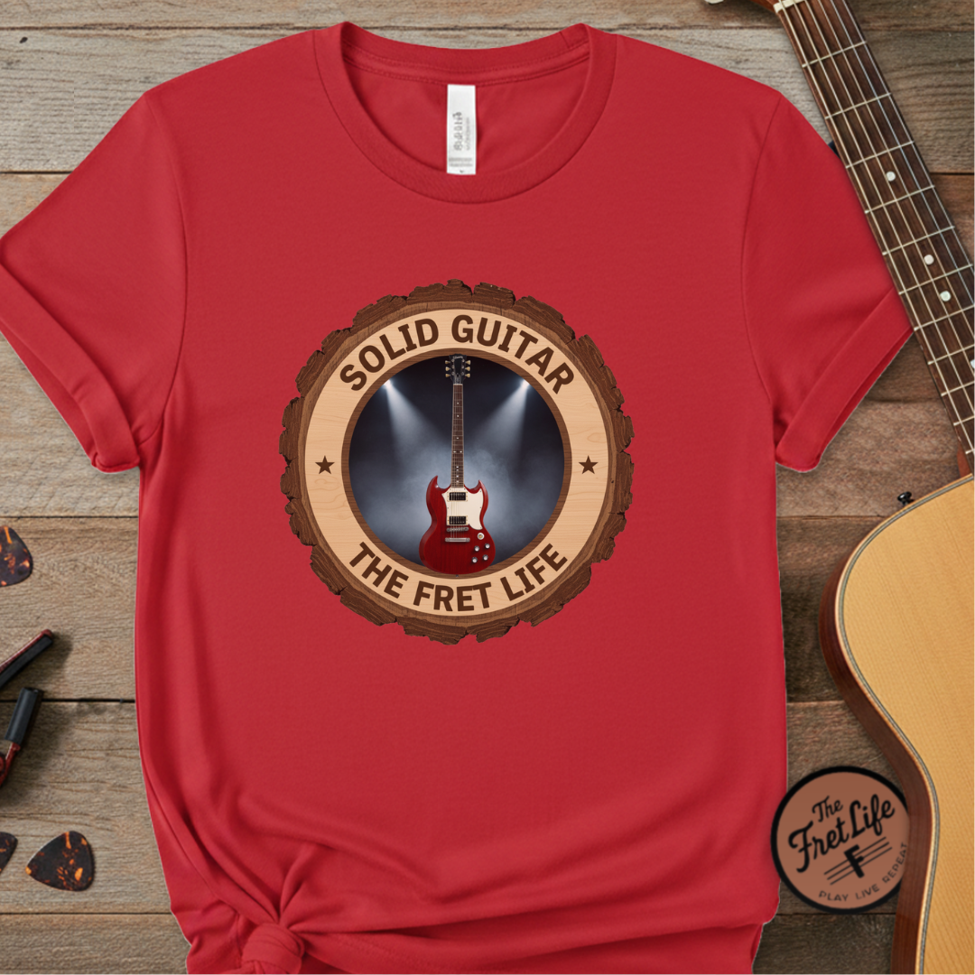Red t-shirt with 'Solid Guitar The Fret Life' design on a wooden surface with a guitar.
