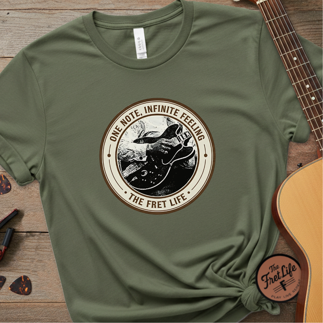 Green t-shirt with 'The Fret Life' graphic design on a wooden surface with a guitar.