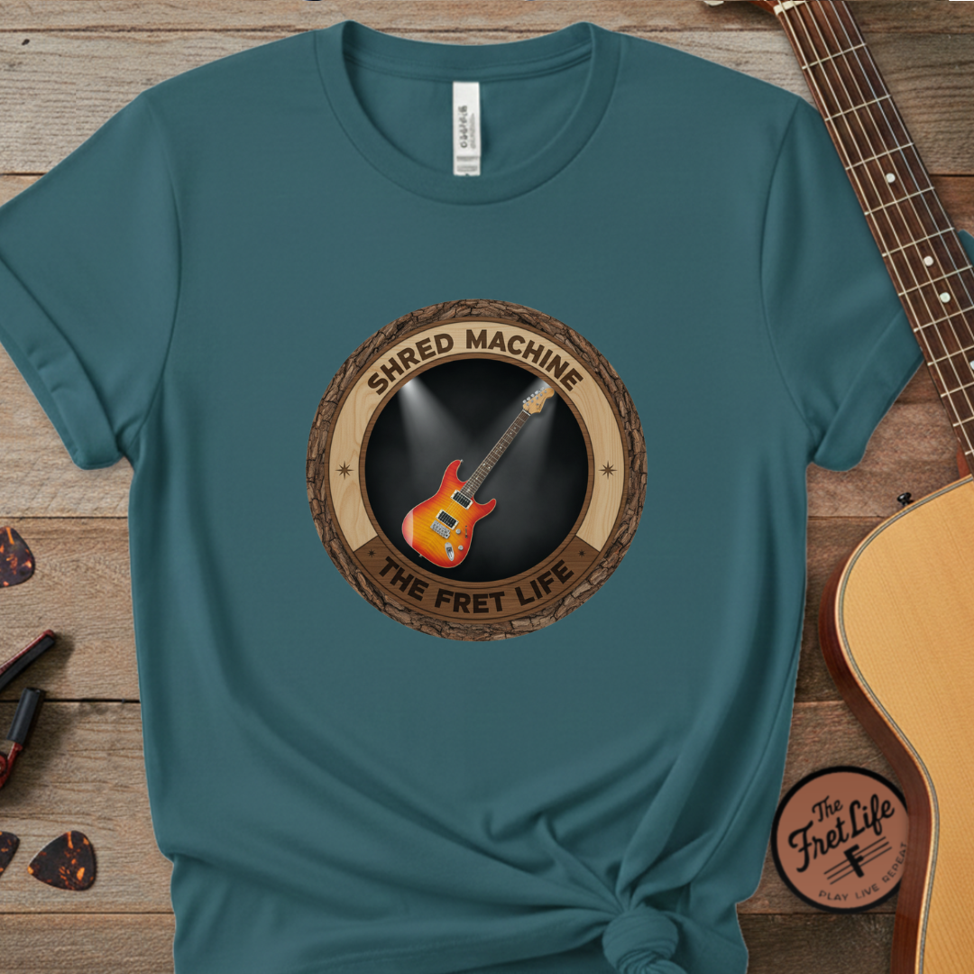 Teal t-shirt with 'Shred Machine' graphic on a wooden surface with a guitar