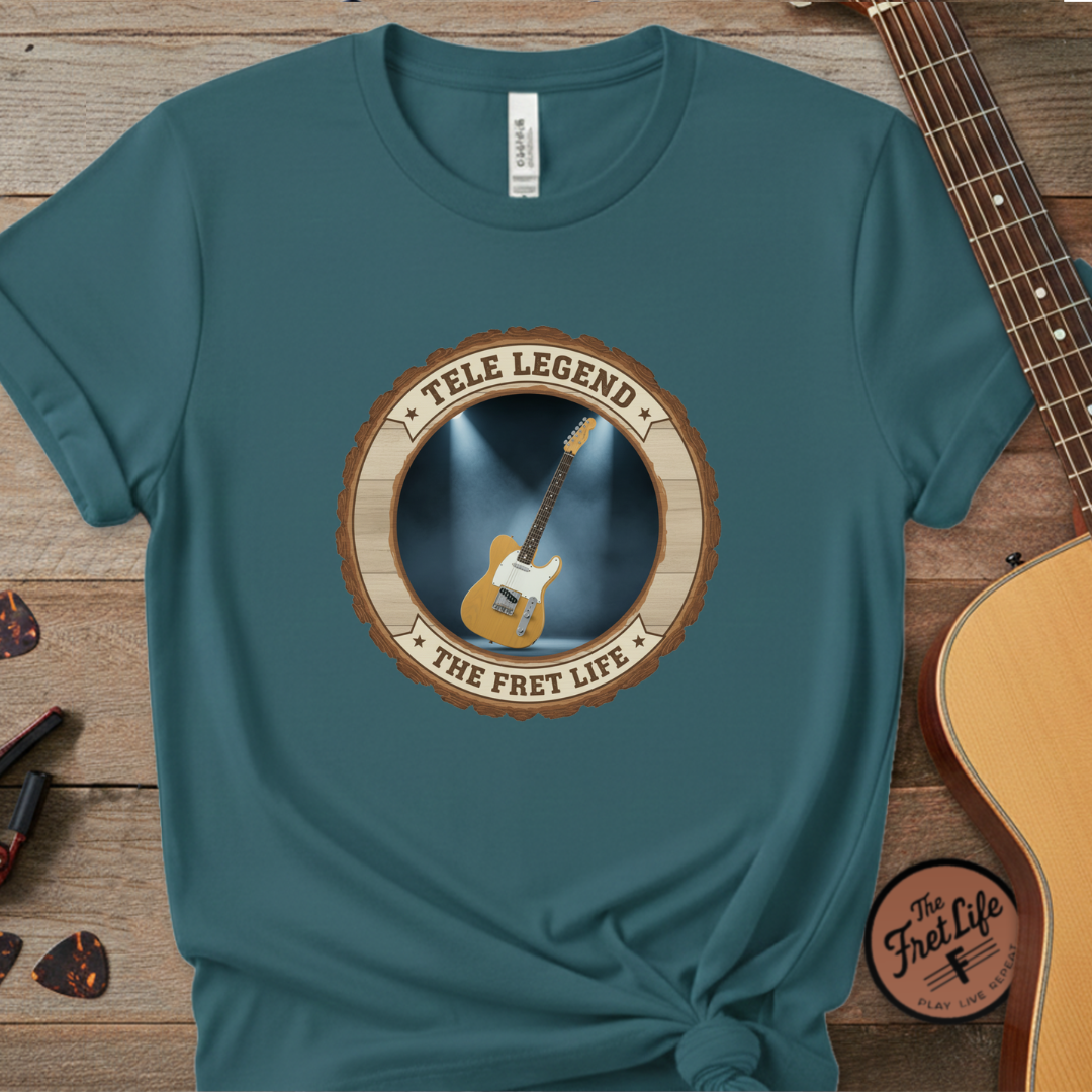 Teal t-shirt with guitar graphic and text on a wooden surface with a guitar.