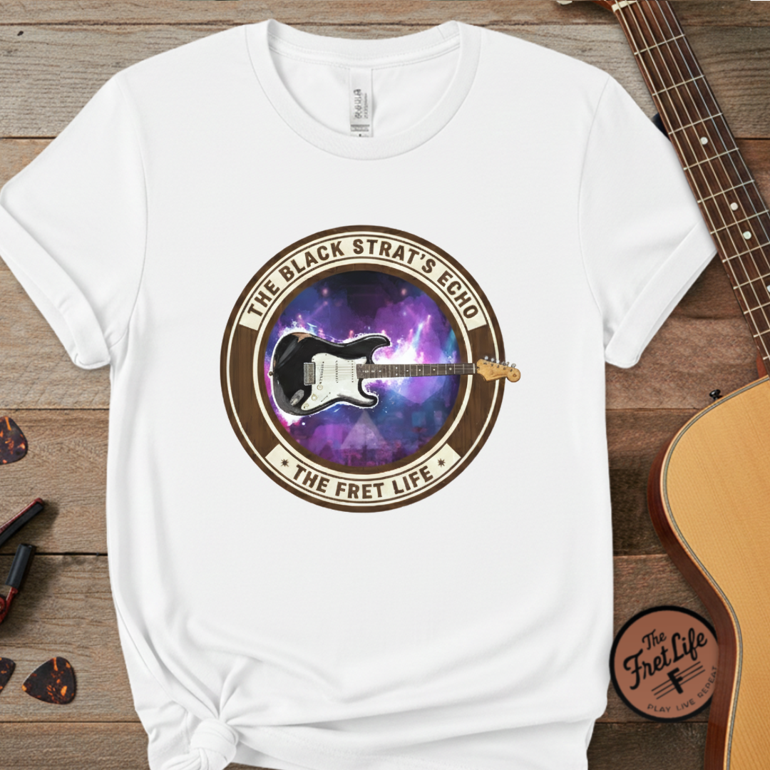 White t-shirt with guitar graphic and text on a wooden surface with a guitar and picks.