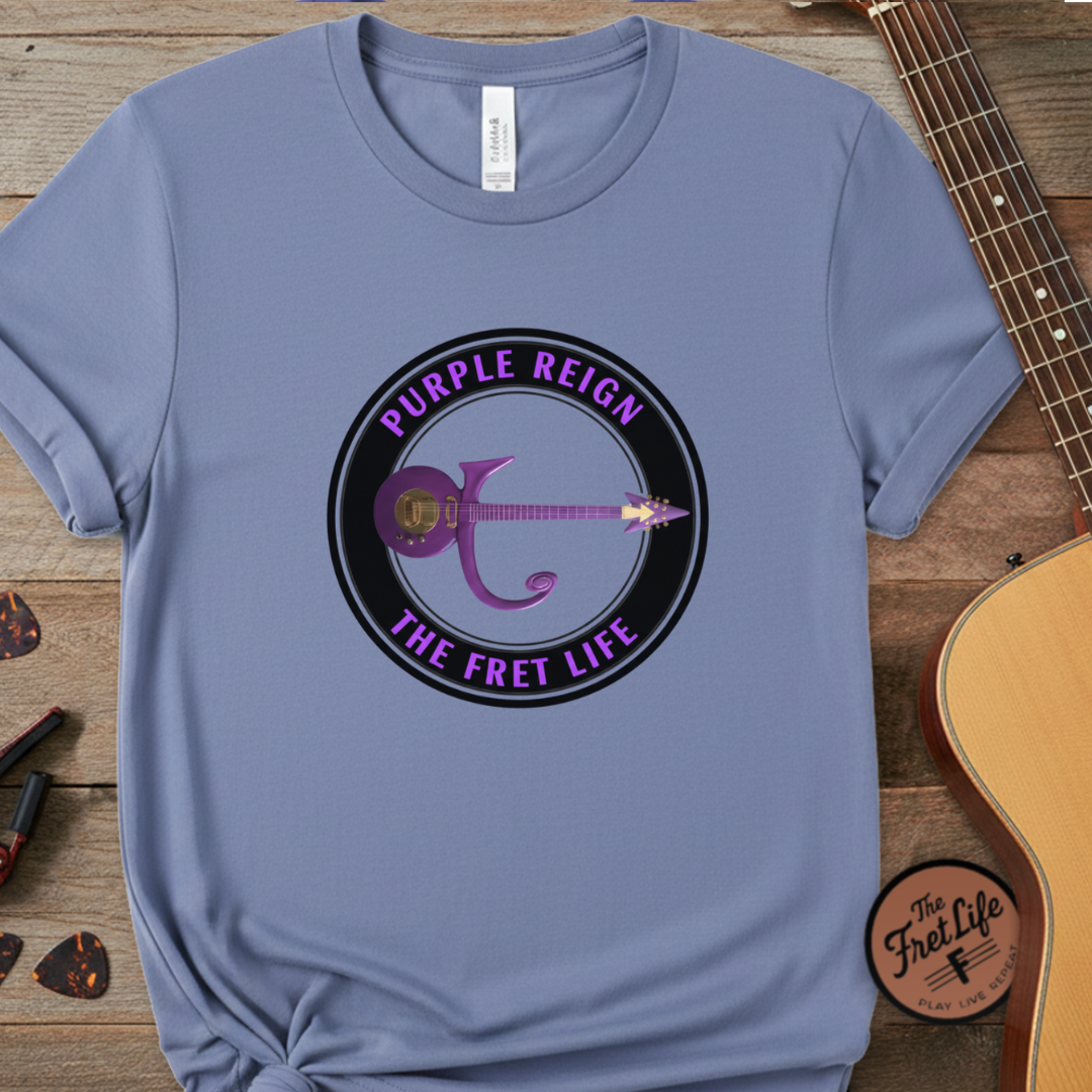 Blue t-shirt with purple guitar graphic and text on a wooden surface with a guitar and pick.