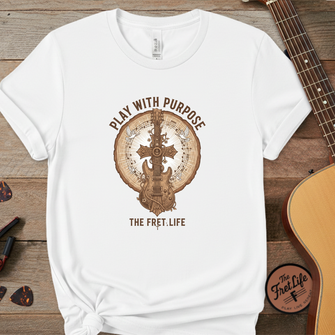 White t-shirt with guitar graphic and 'Play with Purpose' text on a wooden surface with a guitar.