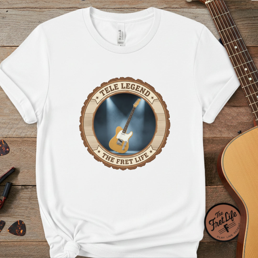 White t-shirt with guitar graphic and 'Tele Legend' text on a wooden surface with a guitar and pick.