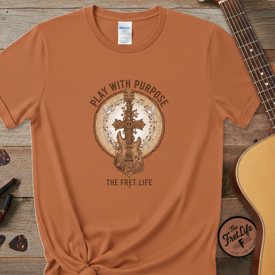 Brown t-shirt with guitar graphic and text on a wooden surface with a guitar and accessories.